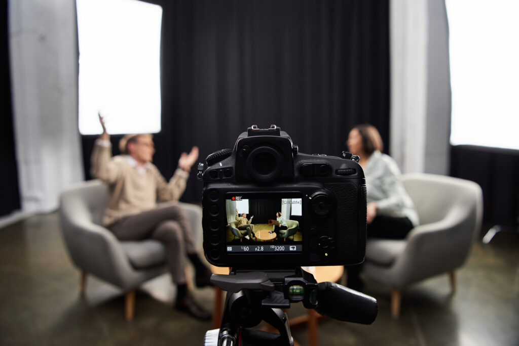 A middle-aged journalist engages in a professional interview with a specialist in a contemporary studio environment.