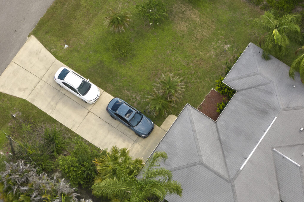 Aerial view of typical contemporary american private house with roof top covered with asphalt shingles and green lawn on yard.